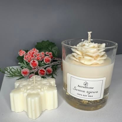Three white soy candles displayed with pink flowers, featuring a flower-shaped candle, a jar candle with wooden wick, and decorative greenery