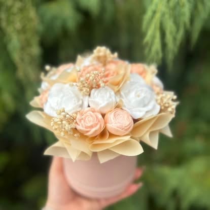 Hand holding a small floral arrangement with white and peach soap flowers in a pink cylindrical box