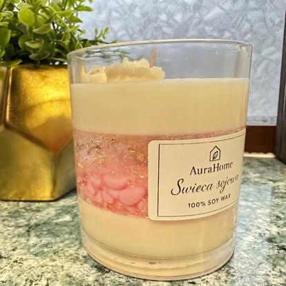 Layered soy wax candle in glass jar with AuraHome label, cream and rose pink layers, next to potted plant
