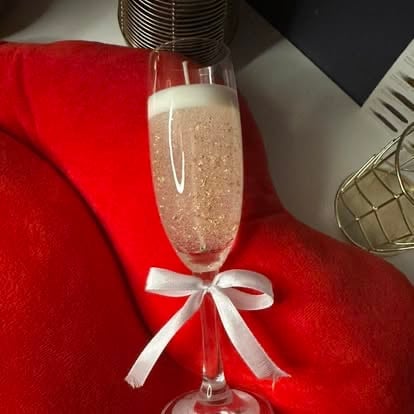 Champagne flute with sparkling rose wine tied with white ribbon bow on red fabric