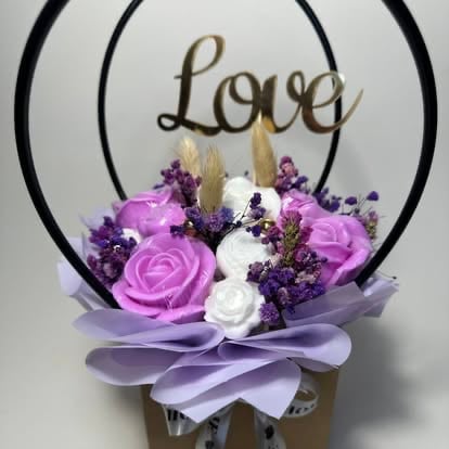 Floral arrangement with purple and white roses, purple berries, and dried pampas grass in a vase with Love sign and black metal arch
