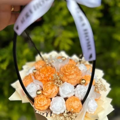 Bouquet of orange and white roses with babys breath wrapped in white paper and tied with a purple ribbon