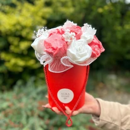 Hand holding a red luxury flower box with pink and white roses adorned with pearl details and a circular Aura label