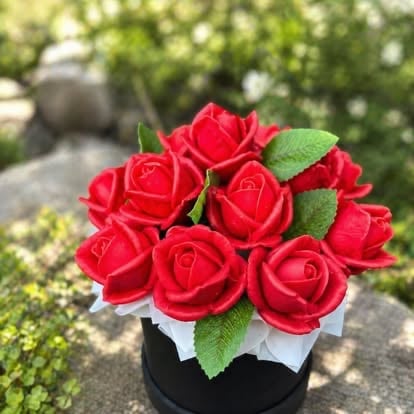 Bouquet of bright red roses with green leaves arranged in a black and white pot in a garden setting