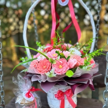Hanging floral arrangement with pink roses, greenery, and burgundy leaves tied with a pink ribbon