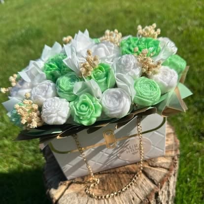 Elegant floral arrangement with white and green roses in a gray quilted box with gold chain handles, displayed on green grass