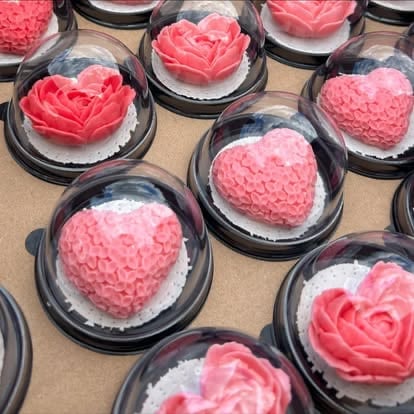 Clear plastic domes containing pink and red decorative flowers and heart-shaped arrangements on a beige surface